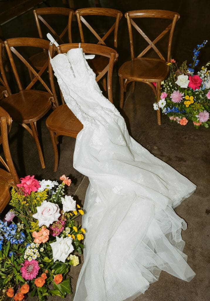 bridal dress laying on chairs with colorful florals next to it